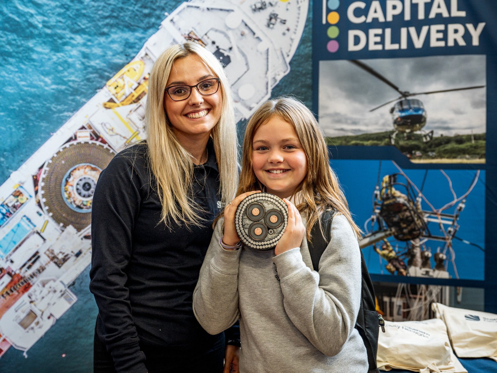 A school pupil holding a cross-section of sub-sea cable, with a member of the team from SSEN