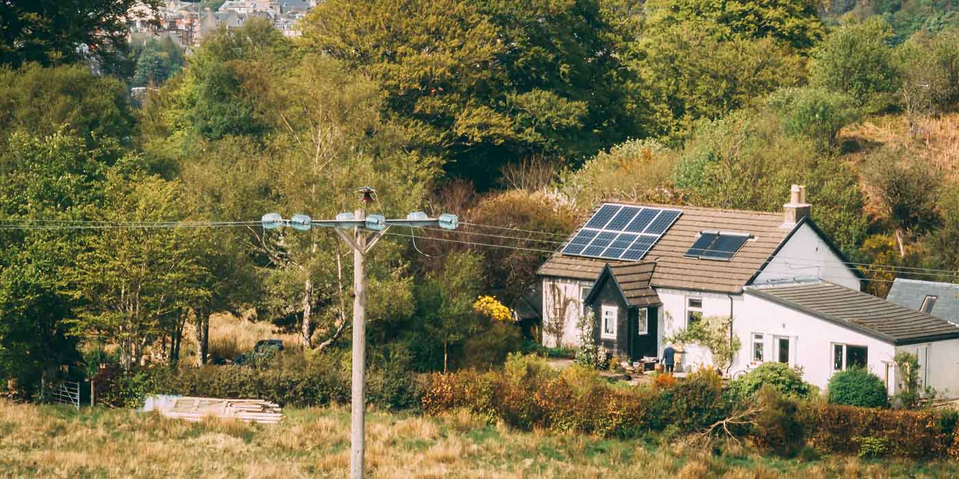 A home in the countryside with solar panels on the roof and a electricity line in front of it