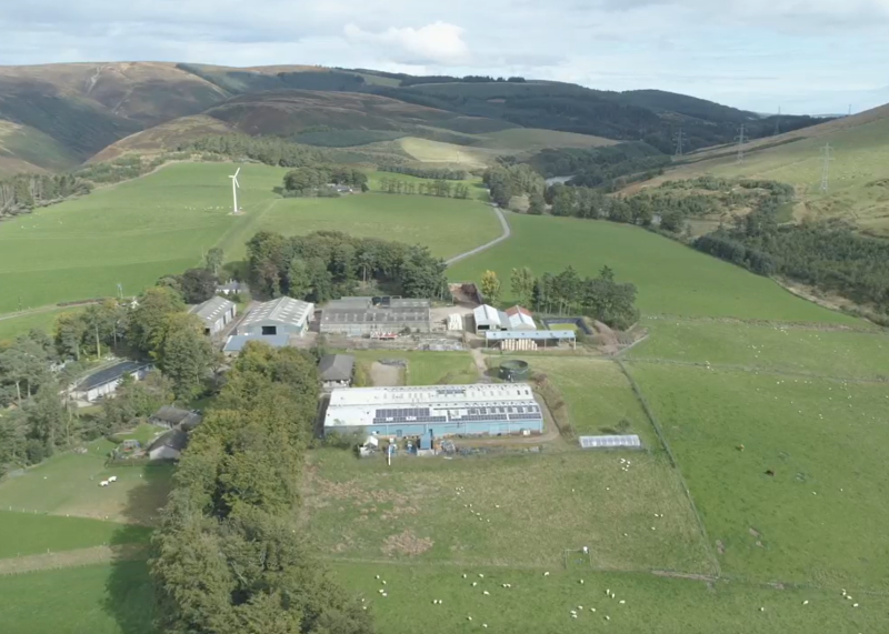 An aerial picture of a farm and farmland with electricity networks and wind turbines in the surrounding landscape