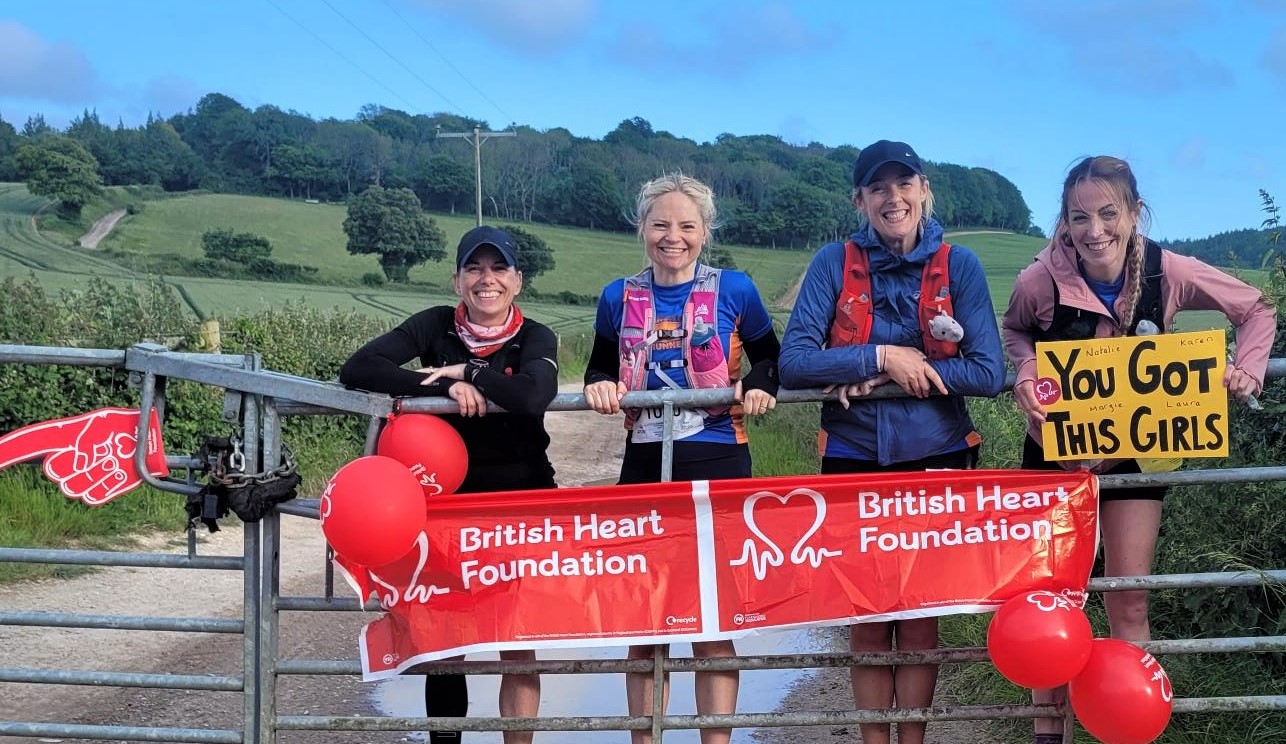 Four female runners standing on a farm gate with balloons and banners