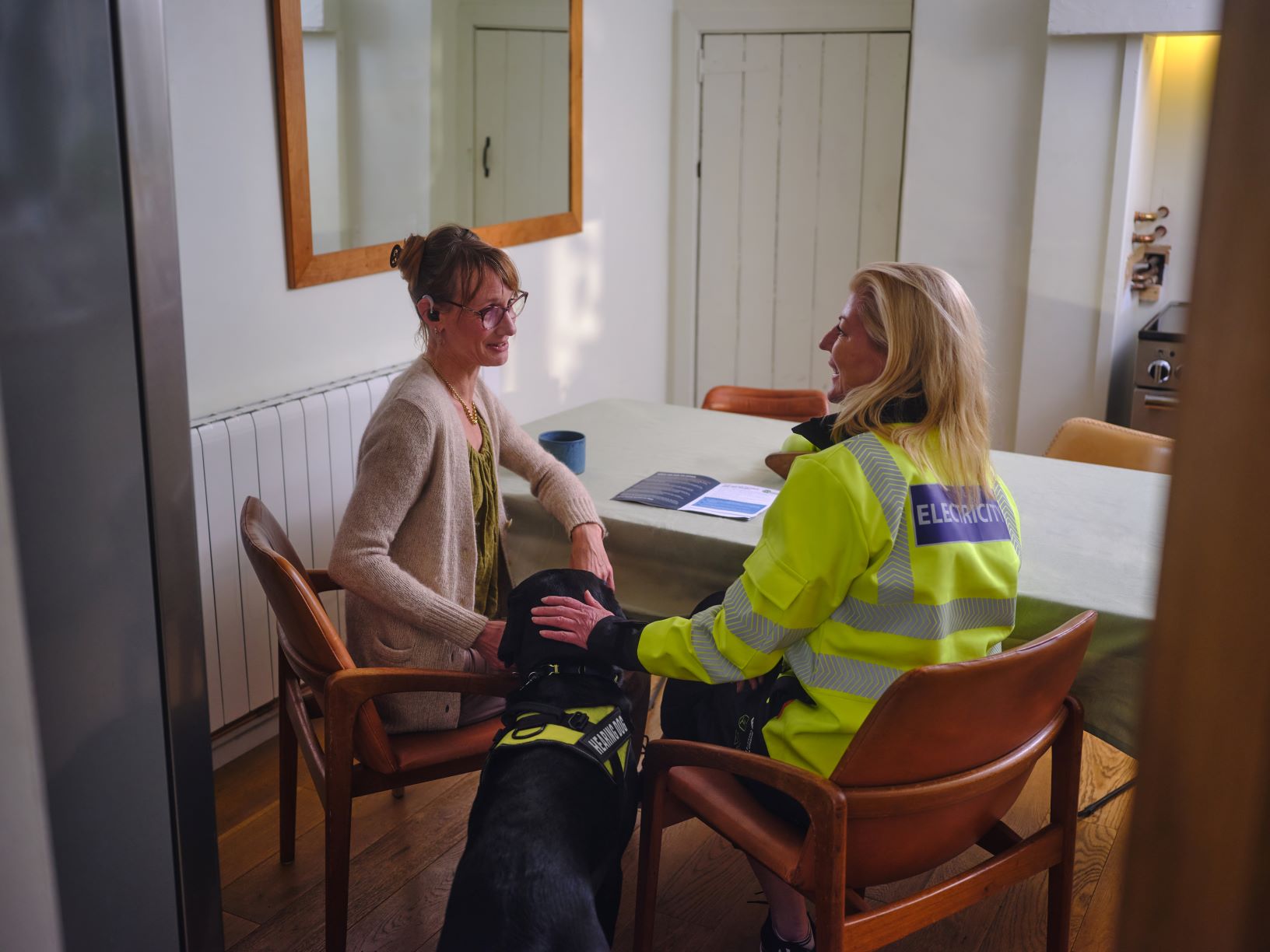 Two women - one in high vis) at kitchen table with guide dog